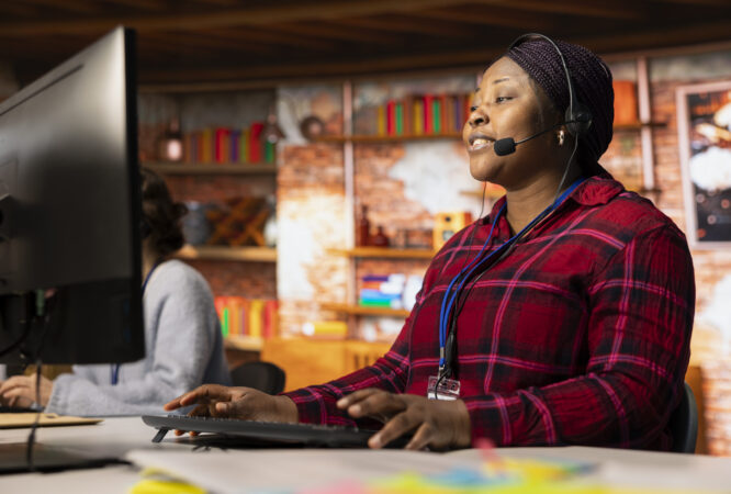 Jolly call center professional typing on PC keyboard, assisting customers through digital communication channels. Friendly customer support representative in live chat with client